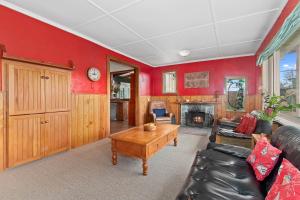 ein Wohnzimmer mit roten Wänden, einem Sofa und einem Tisch in der Unterkunft Beachy Bach - Mangawhai Heads Holiday Home in Mangawhai