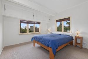 ein weißes Schlafzimmer mit einem Bett und zwei Fenstern in der Unterkunft Beachy Bach - Mangawhai Heads Holiday Home in Mangawhai
