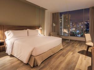a bedroom with a large white bed and a city skyline at Novotel Medellin El Tesoro in Medellín