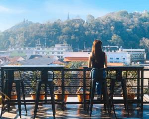 una donna seduta a un tavolo su un balcone che guarda la città di DAAD FAH home and cafe a Phetchaburi