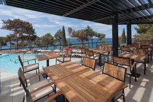 a patio with wooden tables and chairs next to a pool at Hotel Parentium Plava Laguna in Poreč