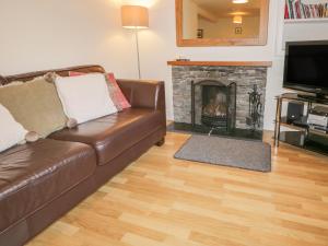 a living room with a brown leather couch and a fireplace at Holly Tree Cottage in Coniston