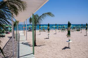 a beach with chairs and palm trees and the ocean at Il Nocchiero City Hotel in Soverato Marina