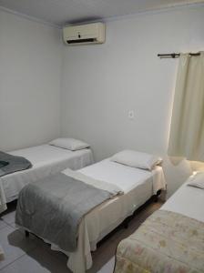 three beds in a room with white walls at Angelu's Hotel in Nova Andradina