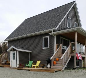 a black house with yellow and green chairs on the porch at BeachView Apartment in Port Hood