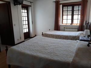 two beds in a bedroom with two windows at Pensão Repouso do Peregrino in Paredes de Coura