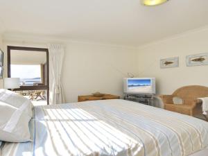 a white bedroom with a bed and a television at Promenade 11 air conditioned unit with beautiful water views in Shoal Bay