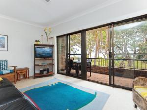ein Wohnzimmer mit einem Sofa, einem TV und einem Balkon in der Unterkunft Sailfish, 4,46 Magnus Street- Unit with water views and close to town in Nelson Bay