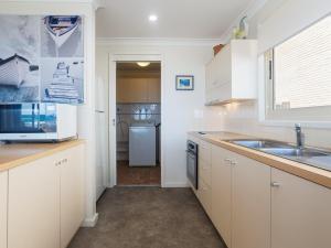 una cucina con armadi bianchi, lavandino e frigorifero di The Whale Watcher waterfront unit with stunning views level access ad Anna Bay