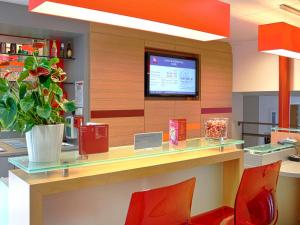 a lobby with a counter with red chairs and a tv at ibis Roscoff in Roscoff