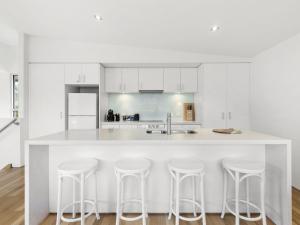 una cocina con armarios blancos y una isla blanca con taburetes en Surf Central, en Lorne