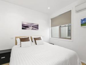 a white bedroom with a large bed and a window at Waterfront Three in Lorne