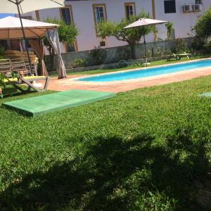 eine grüne Matte neben einem Pool mit Sonnenschirm in der Unterkunft Cerro da Janela Hostel in Alte