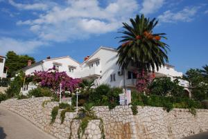 a white house with a palm tree and a stone wall at Apartments & rooms Mila in Banjol