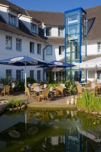 eine Terrasse mit Stühlen und Sonnenschirmen neben einem Teich in der Unterkunft Hotel Wikingerhof in Kropp