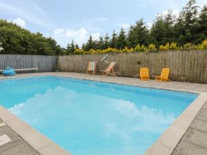 a swimming pool with two chairs and a fence at Old Stable Cottage in Okehampton