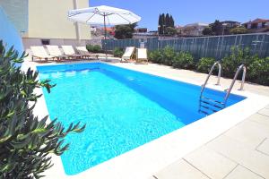 piscina blu con ombrellone e sedie di Sun Apartments a Primošten