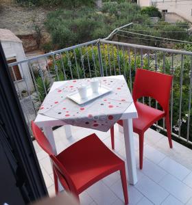 a white table and two red chairs on a balcony at Casetta "Le Due Palme" in Castellammare del Golfo