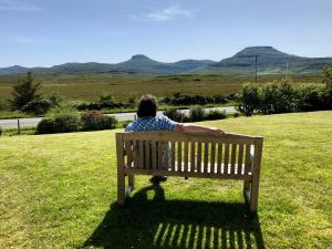 una persona seduta su una panchina in un campo di Kilmuir Park a Dunvegan