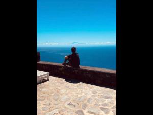 una persona sentada en una pared mirando al océano en Villas Los Torres II en Fuencaliente de la Palma