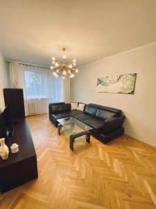 a living room with a black leather couch and a chandelier at Przytulne mieszkanie na Przymorzu w Gdańsku in Gdańsk