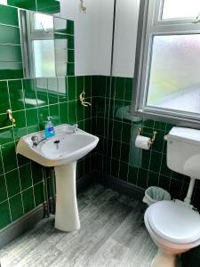 Baño de azulejos verdes con lavabo y aseo en Manchester Stay Hotel, en Mánchester