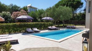 uma piscina com cadeiras e guarda-sóis num quintal em Villa Merra em Premantura