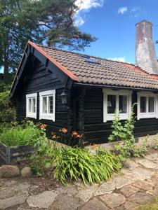 una pequeña casa negra con ventanas y plantas blancas en Havsnära 1700-tals Timmerstuga, en Ängelholm