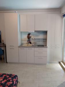 Studio Alezzi Beach Resort في مامايا نورد نافورداي: شخص في المطبخ بخزائن بيضاء