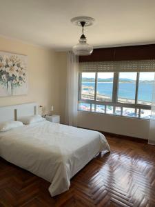 a bedroom with a white bed and a large window at Piso en el malecón de Riveira con vistas a las Rias Baixas. Ideal para familias. 140m in Ribeira