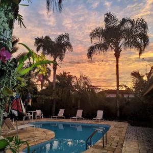 a pool with chairs and palm trees and a sunset at Pousada Na Praia Ubatuba in Ubatuba