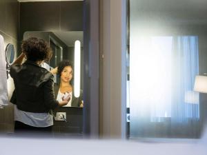 a woman standing in front of a mirror brushing her hair at Novotel RJ Porto Atlantico in Rio de Janeiro