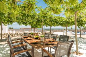 a wooden table and chairs under trees on the beach at Llucasaldentet in Alaior