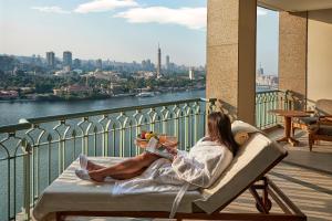 a woman laying in a chair reading a book on a balcony at Four Seasons Hotel Cairo at Nile Plaza in Cairo
