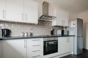 a kitchen with white cabinets and a stainless steel refrigerator at Hullidays - 'Old School Penthouse' Trinity Square in Hull