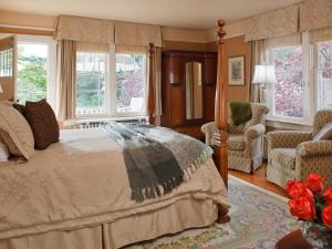 a bedroom with a bed and a chair and windows at Abbeymoore Manor in Victoria