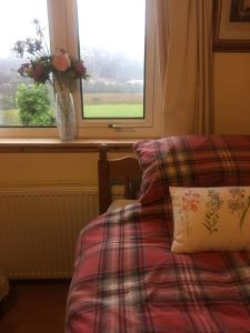 a bed with a pillow and a window with a vase with flowers at Achmore Self catering in Achmore