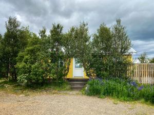 a yellow house with a white door in a yard at Við-Bót Riverside Cottage in Egilsstadir