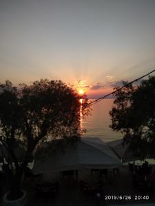 a sunset over the water with a tent and trees at Aktaion in Milína
