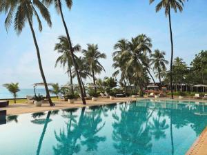 a swimming pool with palm trees and the ocean at Novotel Mumbai Juhu Beach in Mumbai