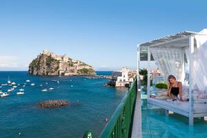 a woman sitting on a bed on a balcony overlooking the ocean at Miramare E Castello in Ischia
