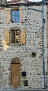 a stone building with wooden shuttered windows and a door at Maison de bourg in Vic-le-Comte