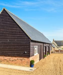 a building with a black roof on a dirt road at Bluebell Cottage at The Old Tractor Barn in Brackley