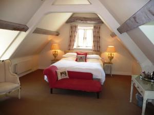 um quarto com uma cama e uma cadeira vermelha em The Swan Inn Swinbrook em Burford