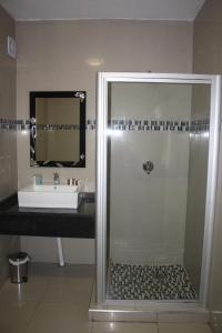 a bathroom with a shower with a sink and a mirror at Oasis Hotel in Mokopane