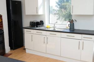 uma cozinha com armários brancos, um lavatório e uma janela em Hullidays - University Side Lg 4 bed House em Hull