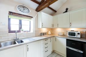 a kitchen with white cabinets and a clock on the wall at Skipbridge Farm Cottages in Green Hammerton