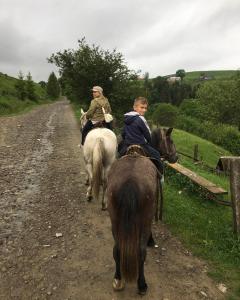 two people riding on horses down a dirt road at Fetal Hut - Плідна Хата in Verkhovyna