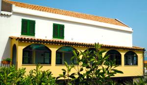 Casa blanca y amarilla con ventanas con contraventanas verdes en Appartamento di Villa Ellizabeth, en Milazzo