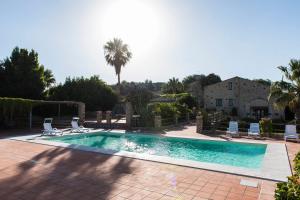 a swimming pool with chairs and a palm tree at Baglio Làuria in Campobello di Licata